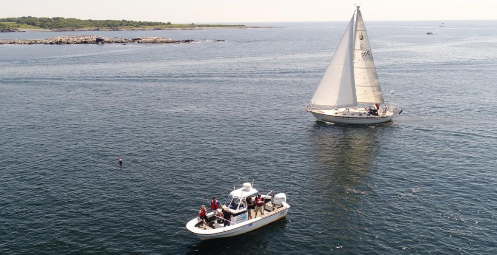 A sailboat and a small vessel move through the Atlantic Ocean off the coast of Maine